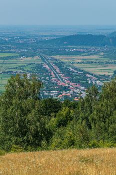 A charming view from the hill to the city lying in a mountain valley with a central street and roofs of houses among the greenery on either side of it.
