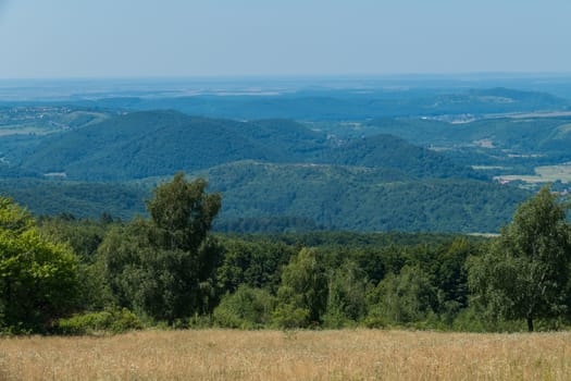 A magnificent landscape of mountainous terrain with green peaks covered with forest bright valleys stretching away to the horizon line.