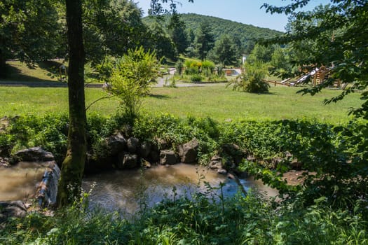 A small river flowing near the hotel complex with a children's playground and a large park area