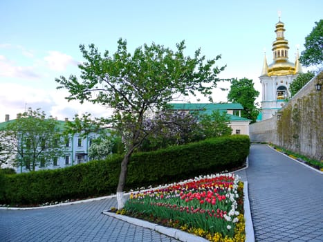 A tiled alley with a triangular flower bed full of multicolored tulips against the church church