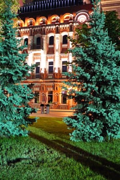 Magnificent view from a green lawn with seated trees on a hotel with beautiful architecture illuminated by evening lights.