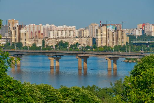 view of the bridge and the area of new buildings with high-rise buildings and chestnuts in the foreground