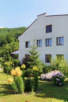 The side wall of the two-story building and the garden behind it with yellow flowers and lawn