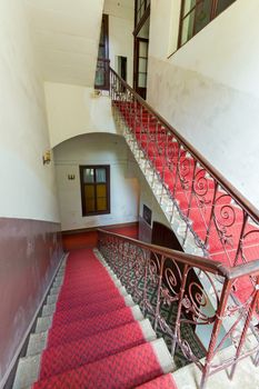 Stair flights in the building between the floors with red carpet. Painted walls and chandeliers in candlesticks on them.