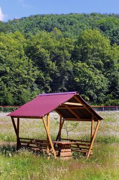 Wooden gazebo with a red roof under a bright scorching summer sun