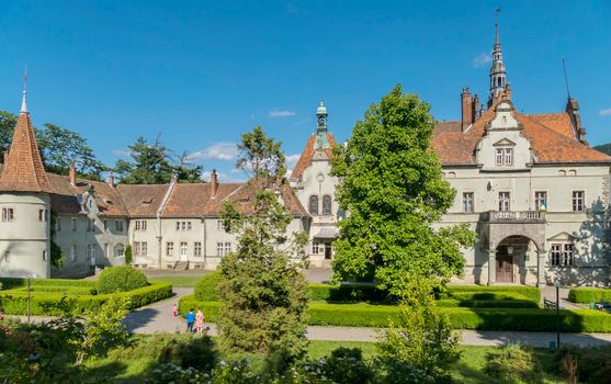 An ancient castle in a beautiful location with a luxurious green courtyard with beautiful lawn paths for walks and bright flowers on the flower beds.