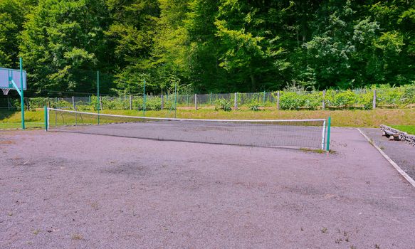Fenced mesh grounds for practicing tennis and basketball against the backdrop of a green forest