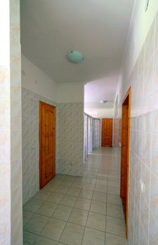 a light corridor surrounded by a tile with a brown wooden door in the locker room