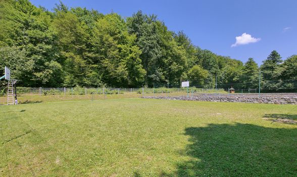 Fields for tennis and basketball with a green lawn against the background of tall trees