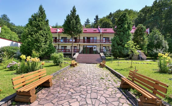 stone trail with wooden benches leading to the hotel on the background of a green mountain
