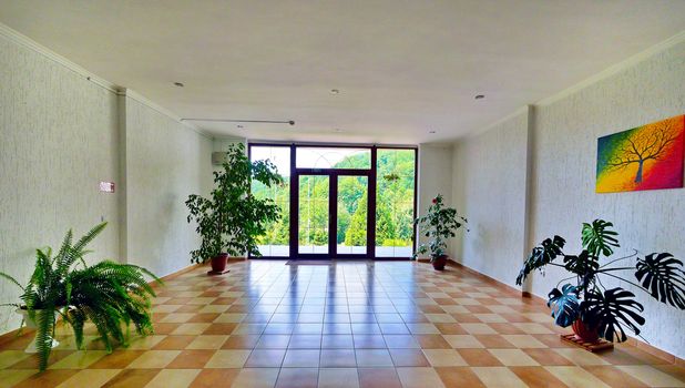 A spacious hall with a balcony, multi-colored tiles on the floor and ornamental plants