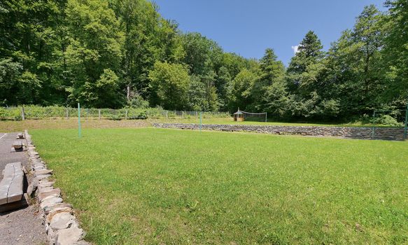 A wide decorative area with a green smoothly trimmed lawn against the backdrop of benches and a wooden pergola in the distance