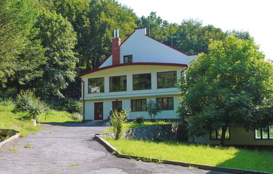 a path from asphalt leading to a two-storey house with a forest growing behind it