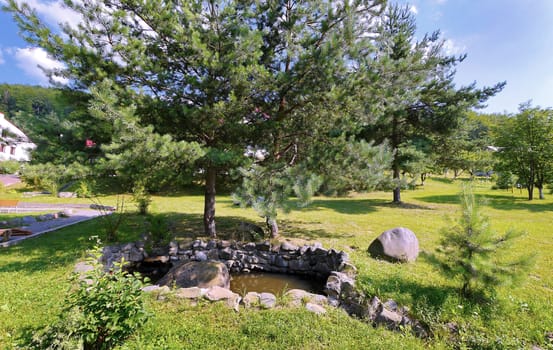 A small decorative lake, surrounded by stones next to large and lush spruce trees