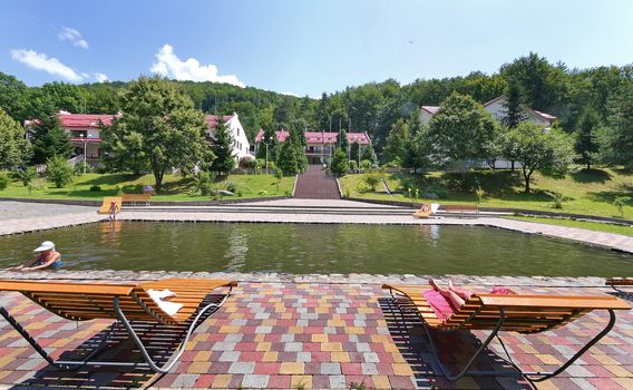 pool with tiled roofs and sun loungers near the hotel complex on the background of green mountains under the blue sky