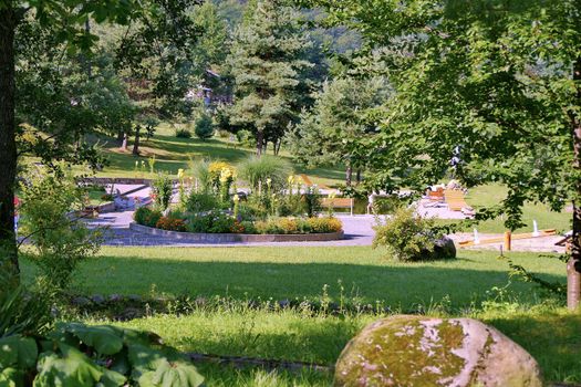 flower bed in a park with benches, with a big stone in the foreground