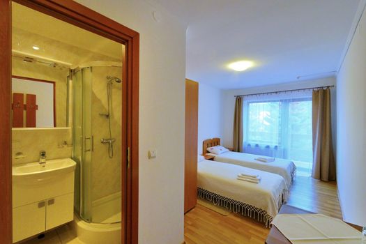 Double room of the hotel with beds covered with white bedspreads and mirrored bathroom with modern renovation.