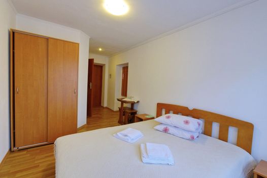 A read hotel room with a bed, covered with a white sheet, a comfortable wardrobe and a table at the entrance