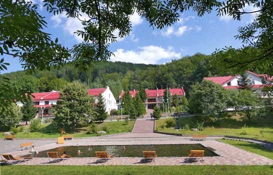 Pool with comfortable wooden sun loungers and benches in the background of the houses of the hotel complex