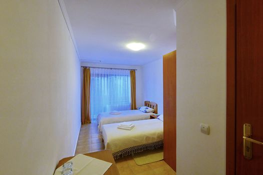 A small clean hotel room with twin beds and a large window