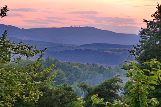 A pink sunset amid the green broad mountains and small houses at their foothills