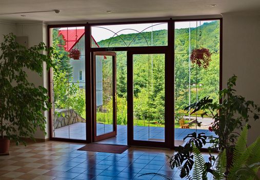 beautiful view from the hall of the building on the lush slopes of the mountains through the wooden door with large windows
