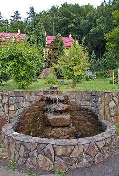 small stone fountain on the background of a lawn with bushes