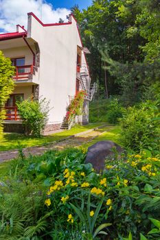 Beautiful view from the flower bed with yellow flowers on the side wall of the hotel with a staircase running along it on the railing of which flowers grow.