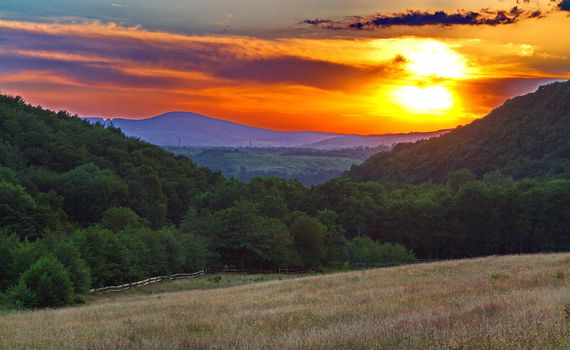 The incredible beauty of the setting sun with a yellow red light over the mountain peaks and beautiful greenery of the coloring nature.