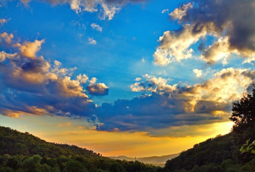 yellow sky under the big clouds in the west over the green mountains