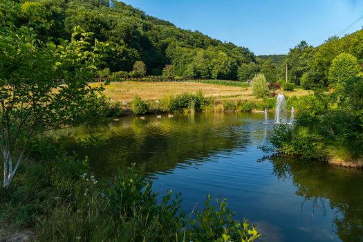 beautiful lake with a fountain and gazebo on the background of green mountains