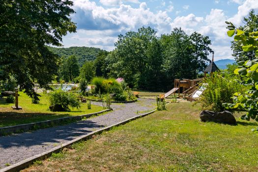 The path leading to the playground near beautiful green flower beds and trees with a swimming pool nearby