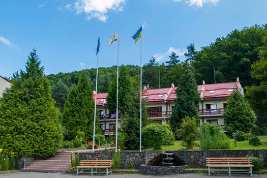 Beautiful two-storey hotel complex with benches and a fountain in the courtyard against the background of green trees