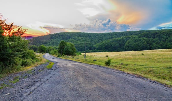 paved road leading to the mountains to the picturesque sunset