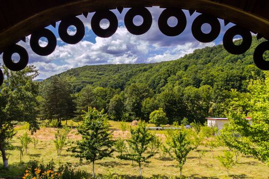 Beautiful view from under the canopy gazebo to the garden with young trees and green mountain slopes against the background of the sky with thick dense clouds.