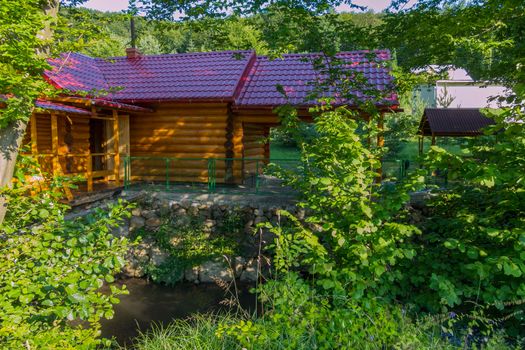 A wooden bath hid in green bushes with a tiled roof in the shade of trees bent their branches over it.
