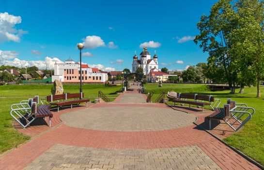 A small rounded garden with comfortable wooden benches against the background of the church church in the distance