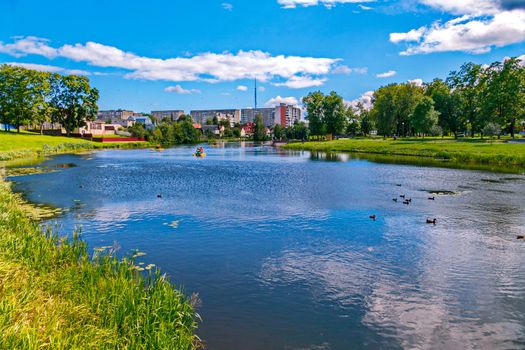 Urban clean pond with green grass around it. There are ducks in it