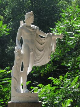 Sculpture of a man in an antique style in a green park surrounded by green trees