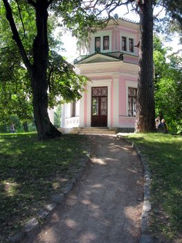 A steep path with two mighty trees on either side leading to a building with pink walls