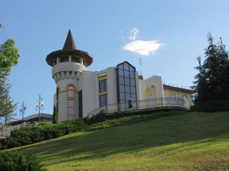 Urban building with a tower on a green hill, against a blue sky