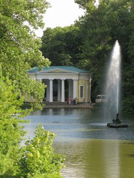 A shooting fountain near a white gazebo with a green roof