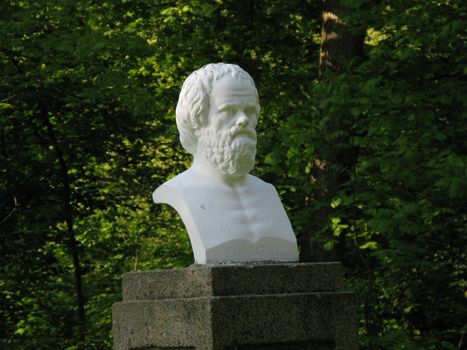 Gypsum bust to a famous historical figure in the background of a park with green trees