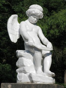 White statue of an angel with small wings, busy with work