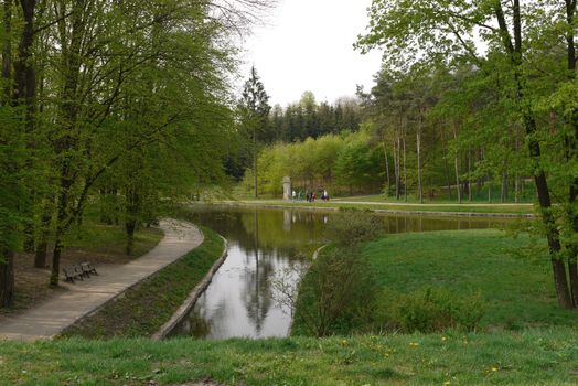 A river near the alley with wooden benches for relaxing in a green park