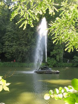 a tall fountain from the mouth of a snake on a stone in the middle of a lake in the park