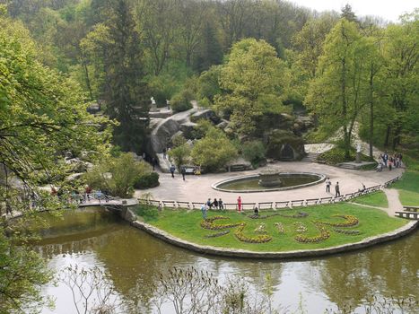 A large number of tourists stroll through the park with green decorative lawns, lakes with bridges and beautiful stone boulders