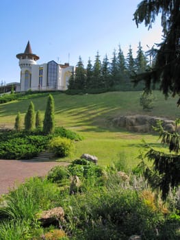 the path of the park against the background of a row of fir trees and a beautiful fairy-tale building