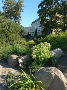 a rocky flowerbed with flowers and bushes near a large bright house