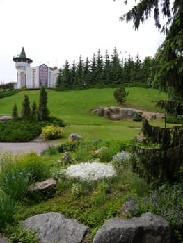 A beautiful landscape of a green park with beautiful slopes with a large variety of shaped stones against the backdrop of a hotel at the top.